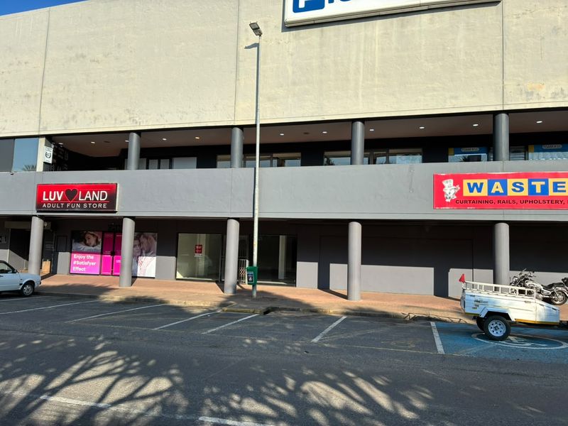 Front elevation of a retail commercial building featuring a paved walkway, structural columns, and multiple storefront units with glass facades.