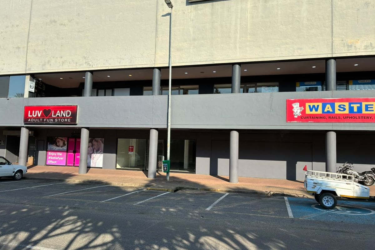 Front elevation of a retail commercial building featuring a paved walkway, structural columns, and multiple storefront units with glass facades.