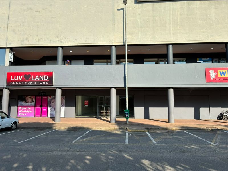 Front elevation of a retail commercial property featuring a paved walkway, concrete support columns, and glass storefronts with parking bays.