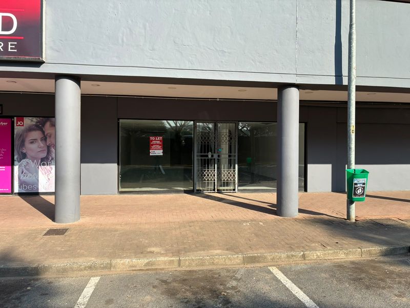Front facade of a retail unit featuring a large glass storefront, security gate, and paved walkway under a covered overhang.
