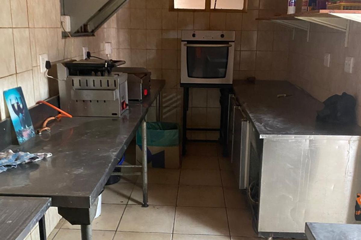 A commercial kitchen prep area featuring stainless steel work surfaces, a built-in oven, extractor fan, and tiled walls and flooring.