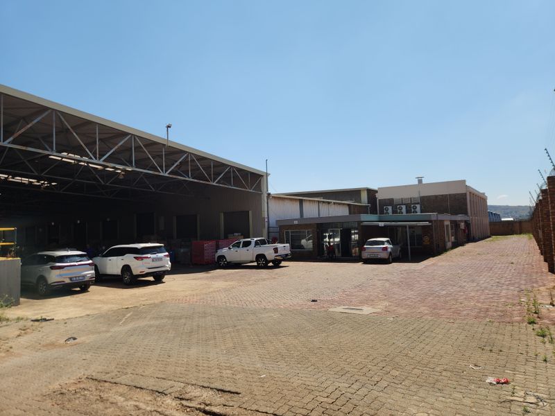 Industrial property featuring a large warehouse structure with steel roof trusses, extensive paved yard space, and perimeter security fencing.