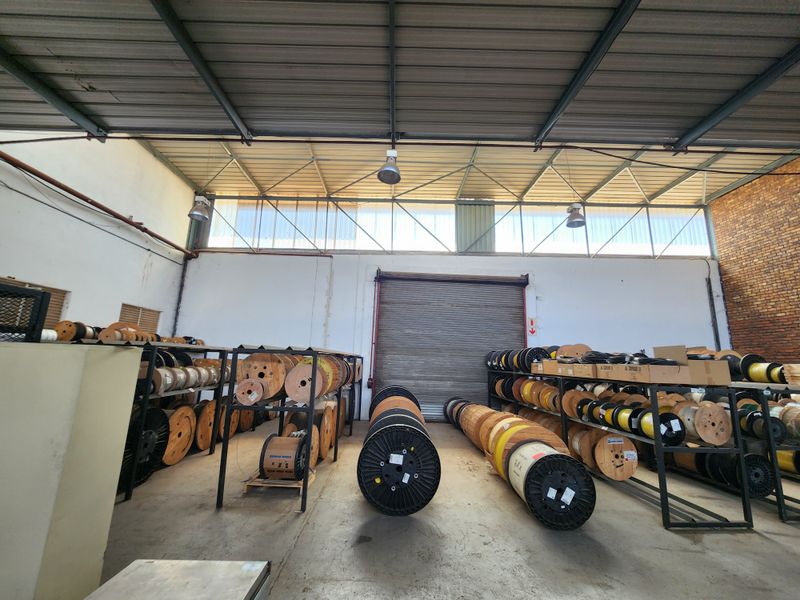 Spacious industrial warehouse unit featuring high ceilings with exposed steel trusses, concrete flooring, and a large roller shutter door for easy access.