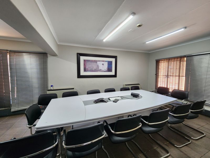 A functional office or boardroom space featuring tiled flooring, fluorescent lighting, and venetian blinds on the windows.