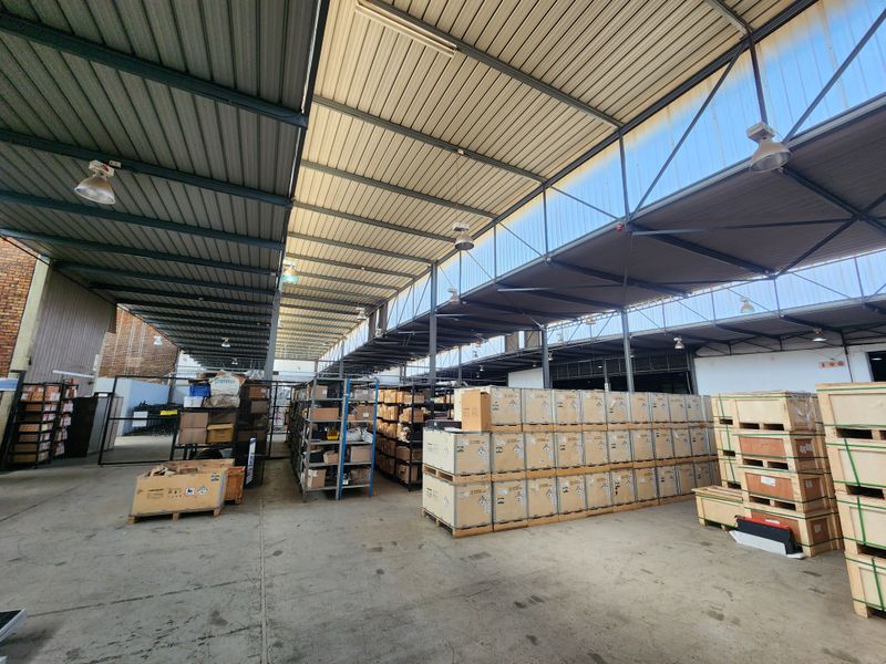 Spacious industrial warehouse area featuring high-clearance corrugated metal roofing, steel truss framework, and durable concrete flooring, suitable for storage or logistics operations.