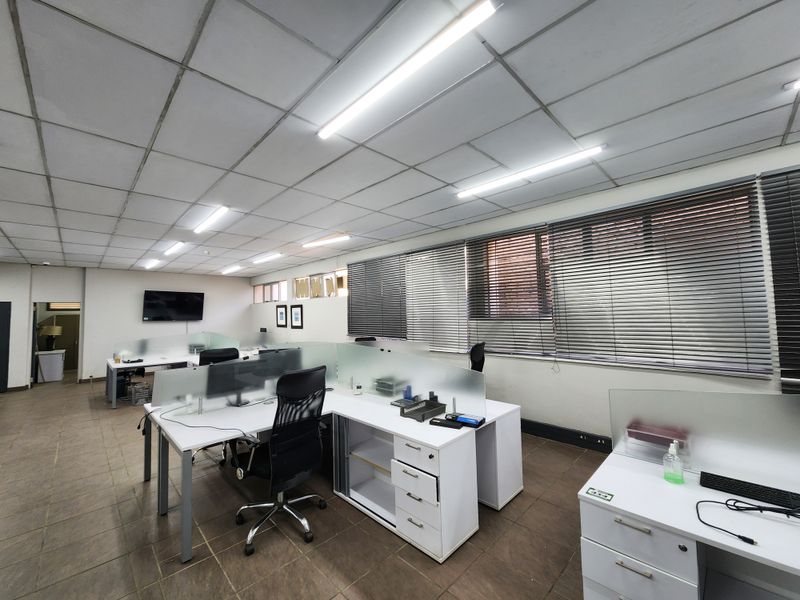 Open-plan office space featuring suspended ceilings, fluorescent lighting, tiled flooring, and built-in desk partitions with privacy screens.