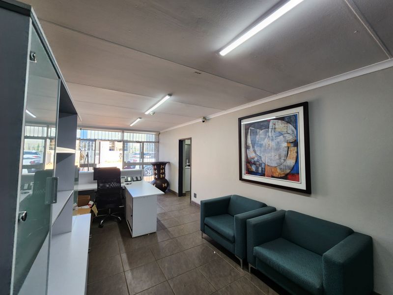A functional office space featuring tiled flooring, fluorescent lighting, and security bars on the windows, providing a professional environment for business operations.
