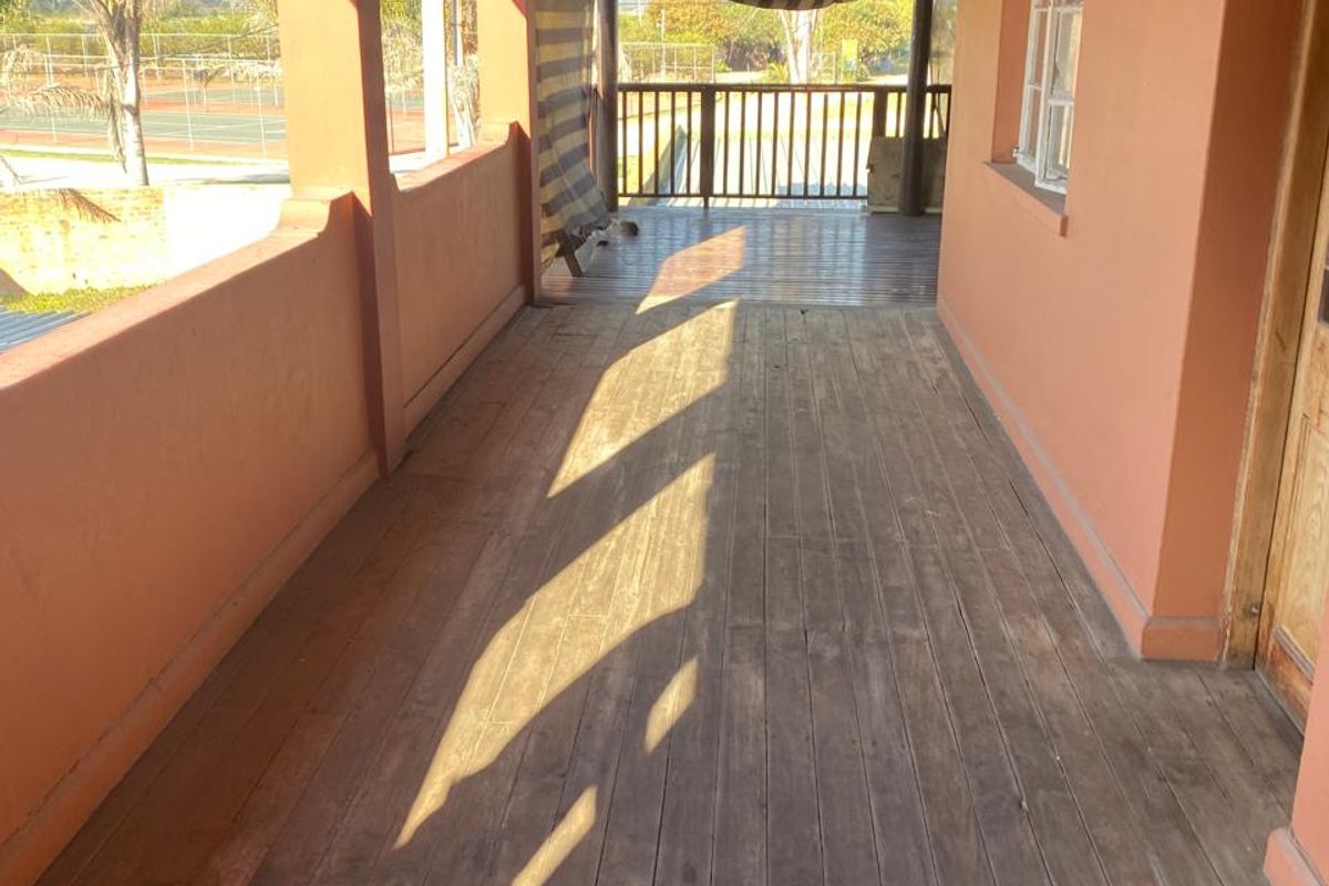 A covered outdoor patio featuring timber decking, exposed beam ceiling, and a balustrade, offering views of the surrounding grounds.