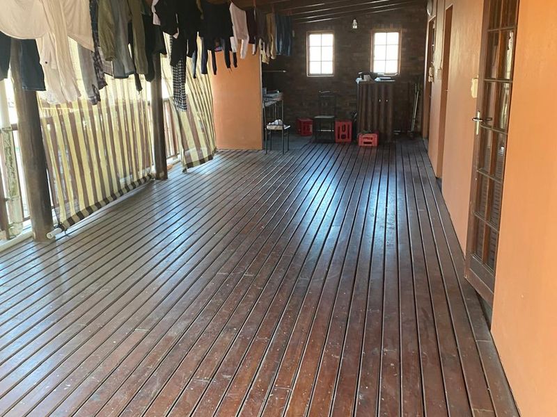 A covered outdoor patio featuring timber decking, exposed wooden roof beams, and access to the main building structure.