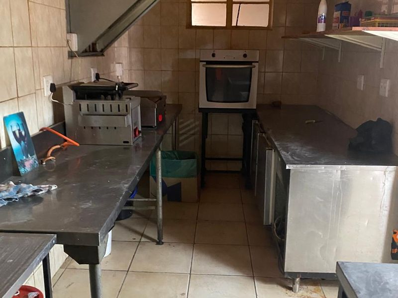 A commercial kitchen prep area featuring stainless steel work surfaces, a built-in oven, extractor fan, and tiled walls and flooring.