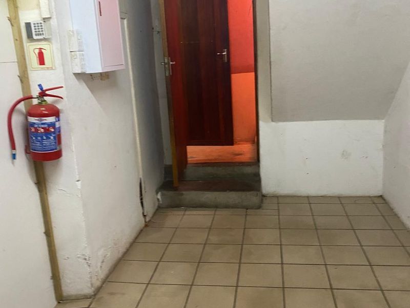 A utilitarian hallway or utility space featuring tiled flooring, a fire extinguisher, and a doorway leading to an adjacent room.