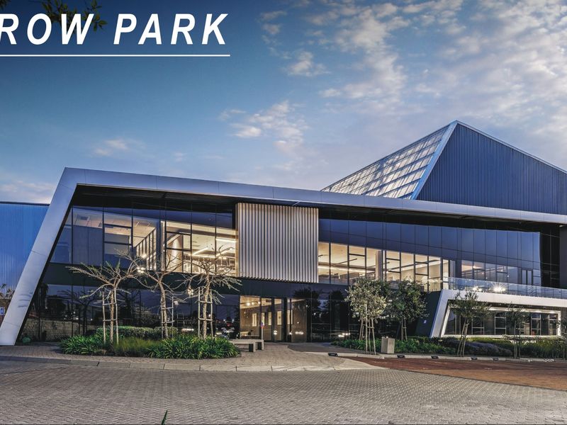 Modern industrial office building facade featuring extensive glass curtain walling, metal cladding, and professional landscaping at the entrance.