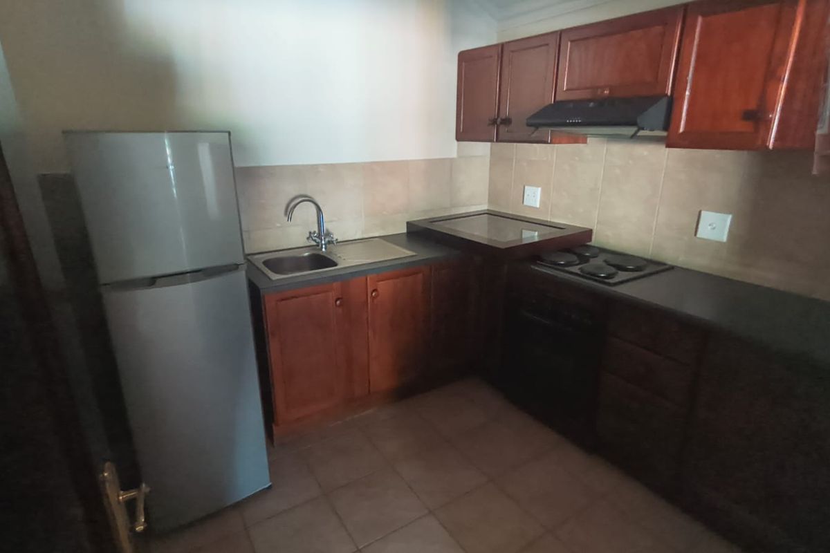 A functional kitchen featuring wooden cabinetry, a built-in oven and hob, extractor fan, and tiled backsplash.