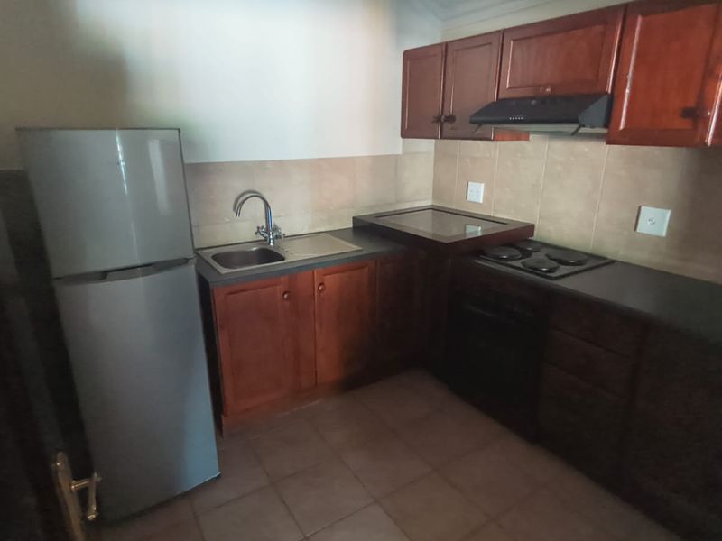 A functional kitchen featuring wooden cabinetry, a built-in oven and hob, extractor fan, and tiled backsplash.