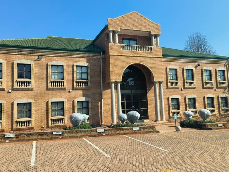 Front elevation of a two-story brick office building featuring an arched entrance, columns, and a paved parking area.