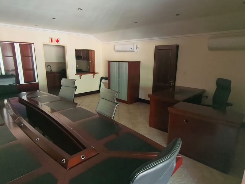 Spacious office area featuring tiled flooring, dual air conditioning units, recessed lighting, and a convenient serving hatch connecting to an adjacent kitchenette area.