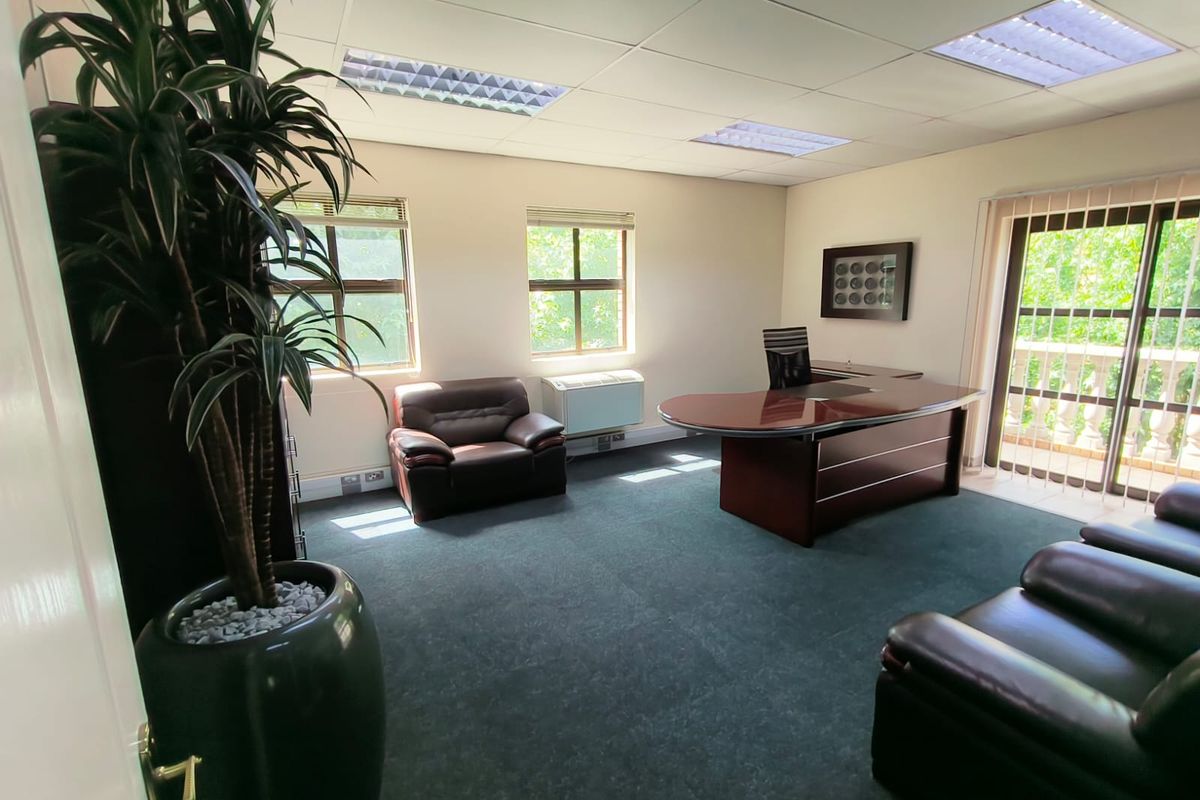 A professional office space featuring a suspended ceiling with recessed lighting, carpeted flooring, and a sliding glass door leading to an outdoor area.