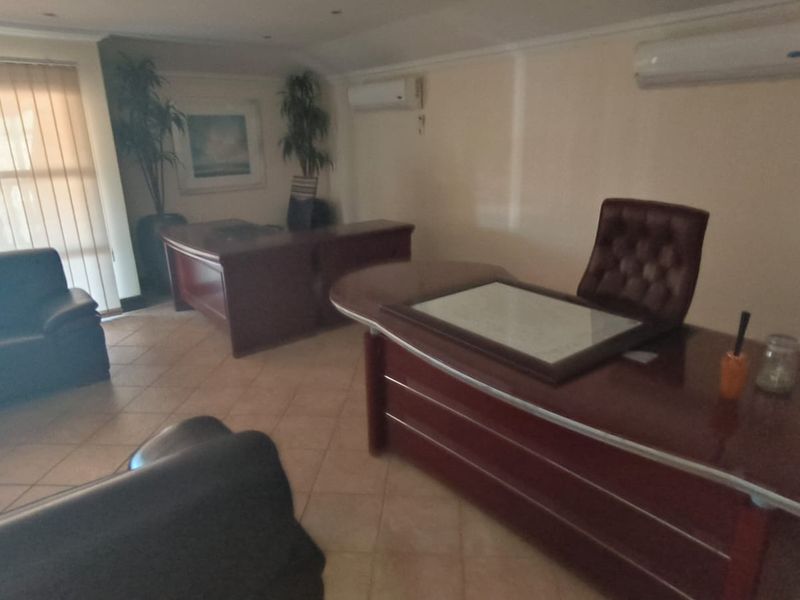 A spacious office area featuring tiled flooring, dual split-system air conditioning units, and large windows with vertical blinds.