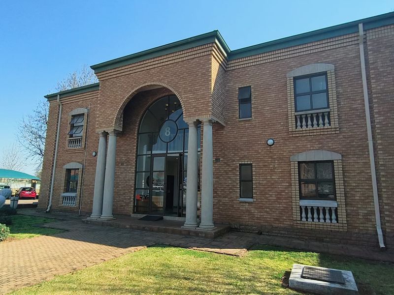 Front elevation of a two-story brick office building featuring an arched entrance with stone columns and paved exterior access.