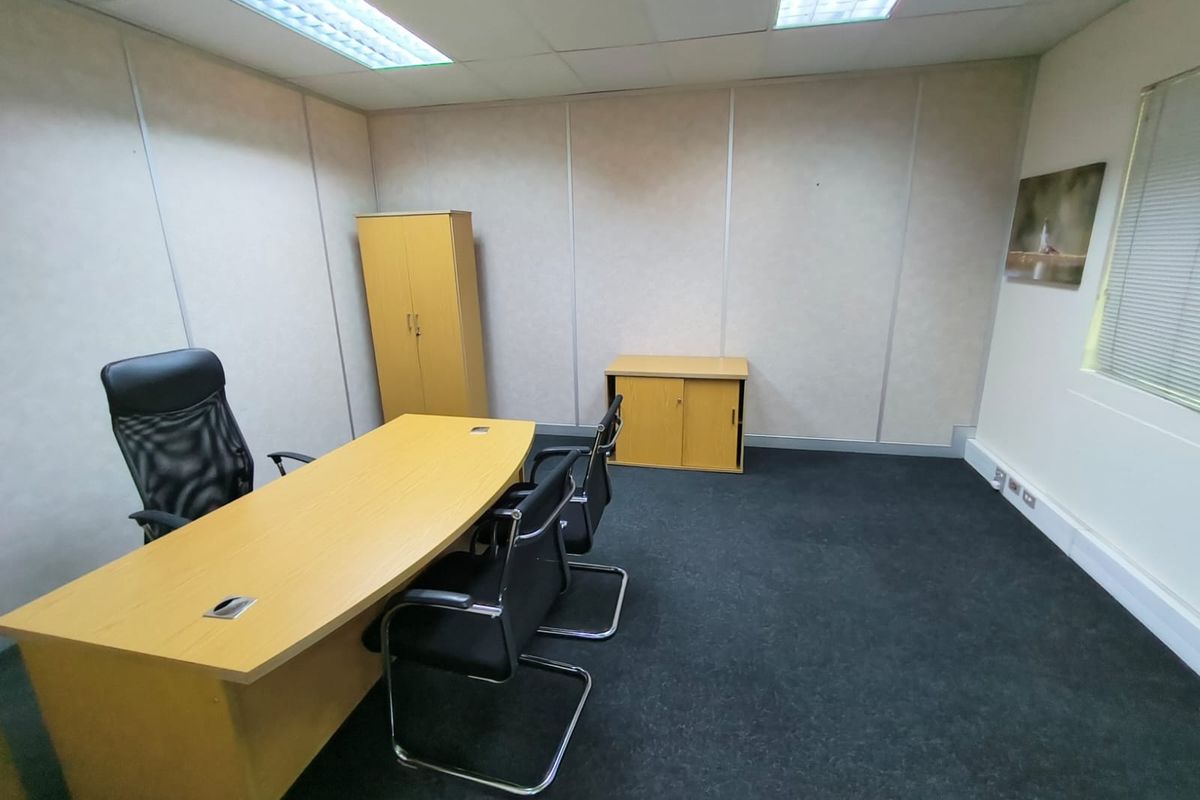 A functional office space featuring modular wall panels, suspended ceiling with recessed lighting, and dark carpet flooring.