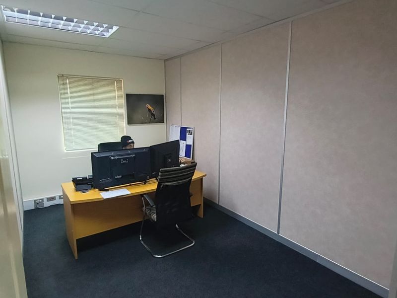 A functional office space featuring carpeted flooring, partition walling, and a suspended ceiling with recessed lighting.