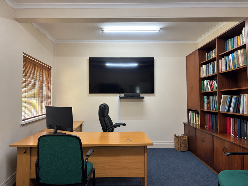 A functional office space featuring built-in wooden cabinetry, carpeted flooring, and venetian blinds, providing a professional environment for work.