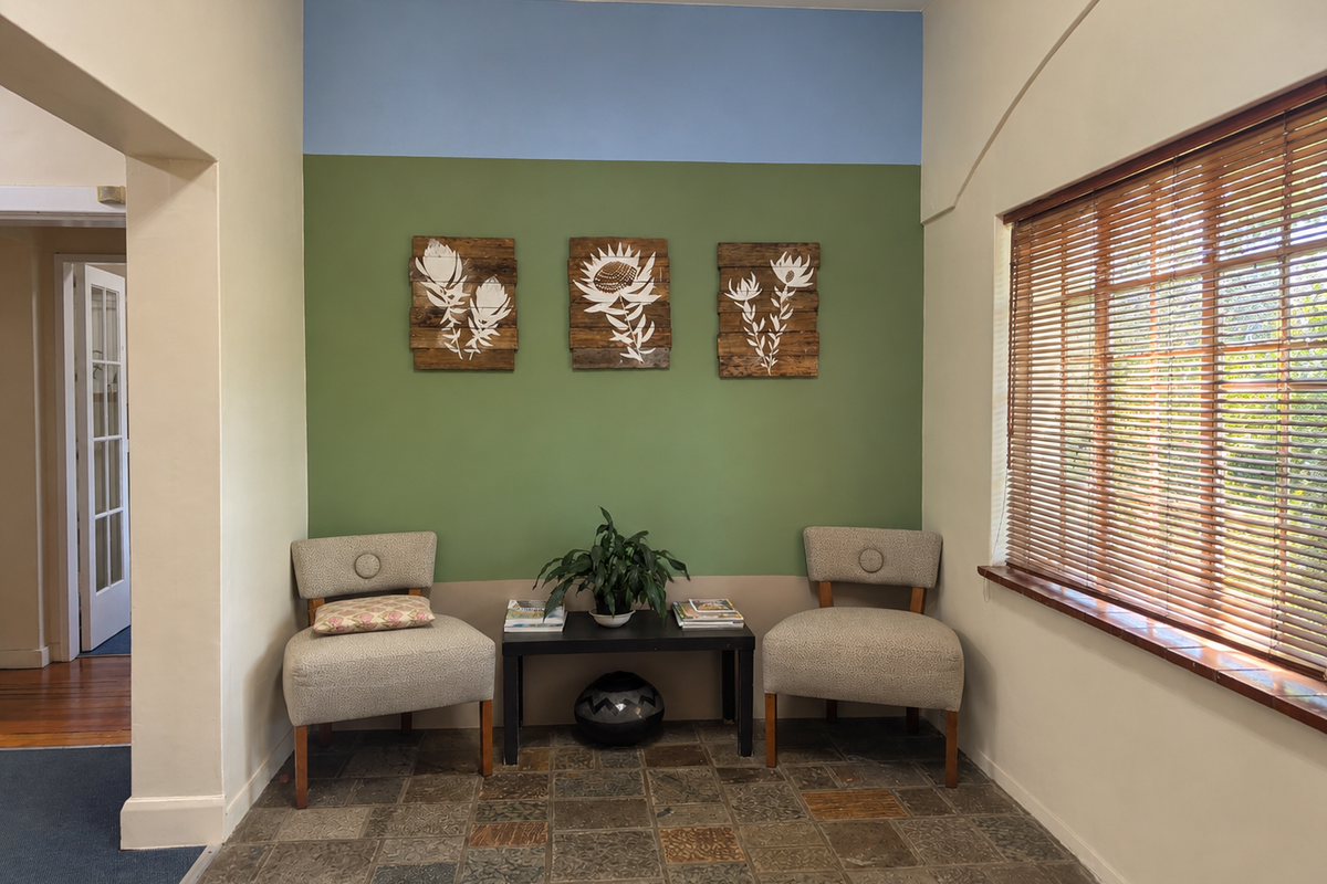 A bright office waiting area featuring natural stone tile flooring, large windows with wooden blinds, and a decorative multi-toned accent wall.