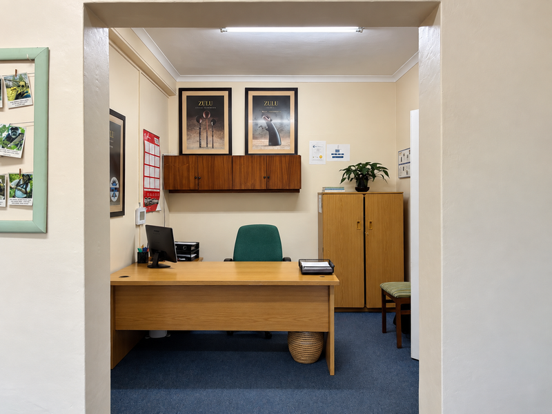 A functional office space featuring built-in wall cabinetry, carpeted flooring, and overhead fluorescent lighting, providing a practical work environment.