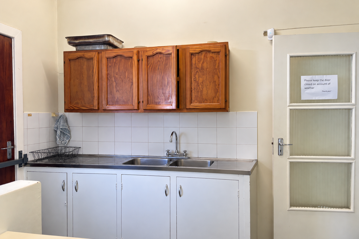 A functional kitchenette featuring a stainless steel double sink, tiled splashback, and a mix of wooden wall cabinets and white base storage units.