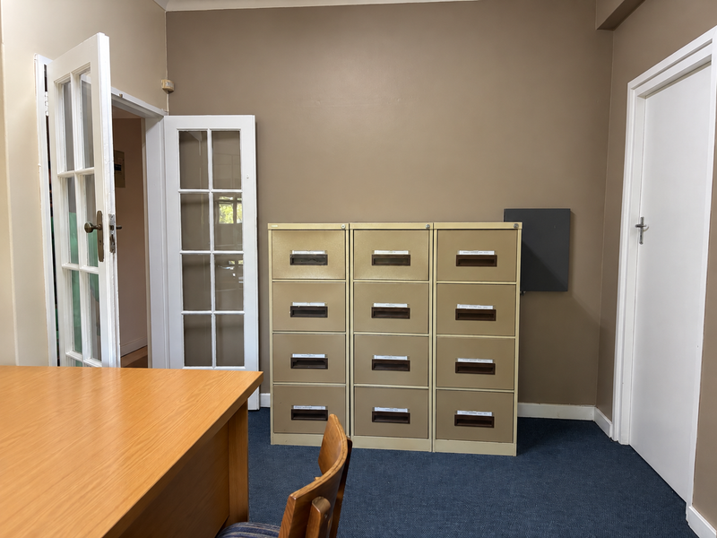 A functional office space featuring carpeted flooring, classic french doors, and neutral wall tones, providing a practical environment for professional use.