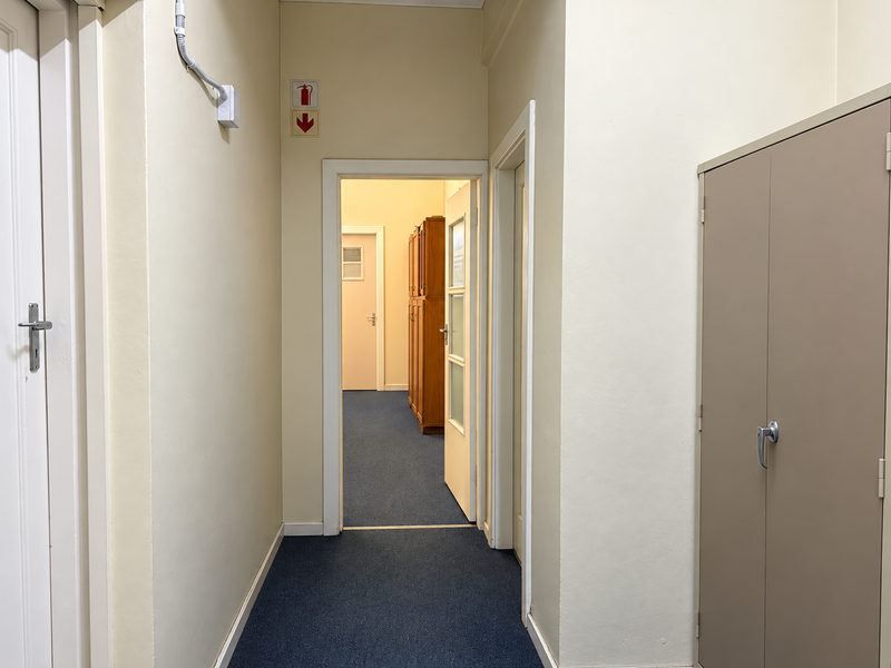 A functional office hallway featuring neutral walls, blue carpeting, and a built-in metal storage cabinet.