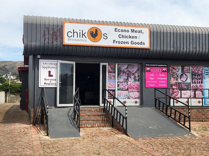 Front elevation of a retail property featuring a metal facade, accessibility ramps with handrails, and large display windows for product advertising.