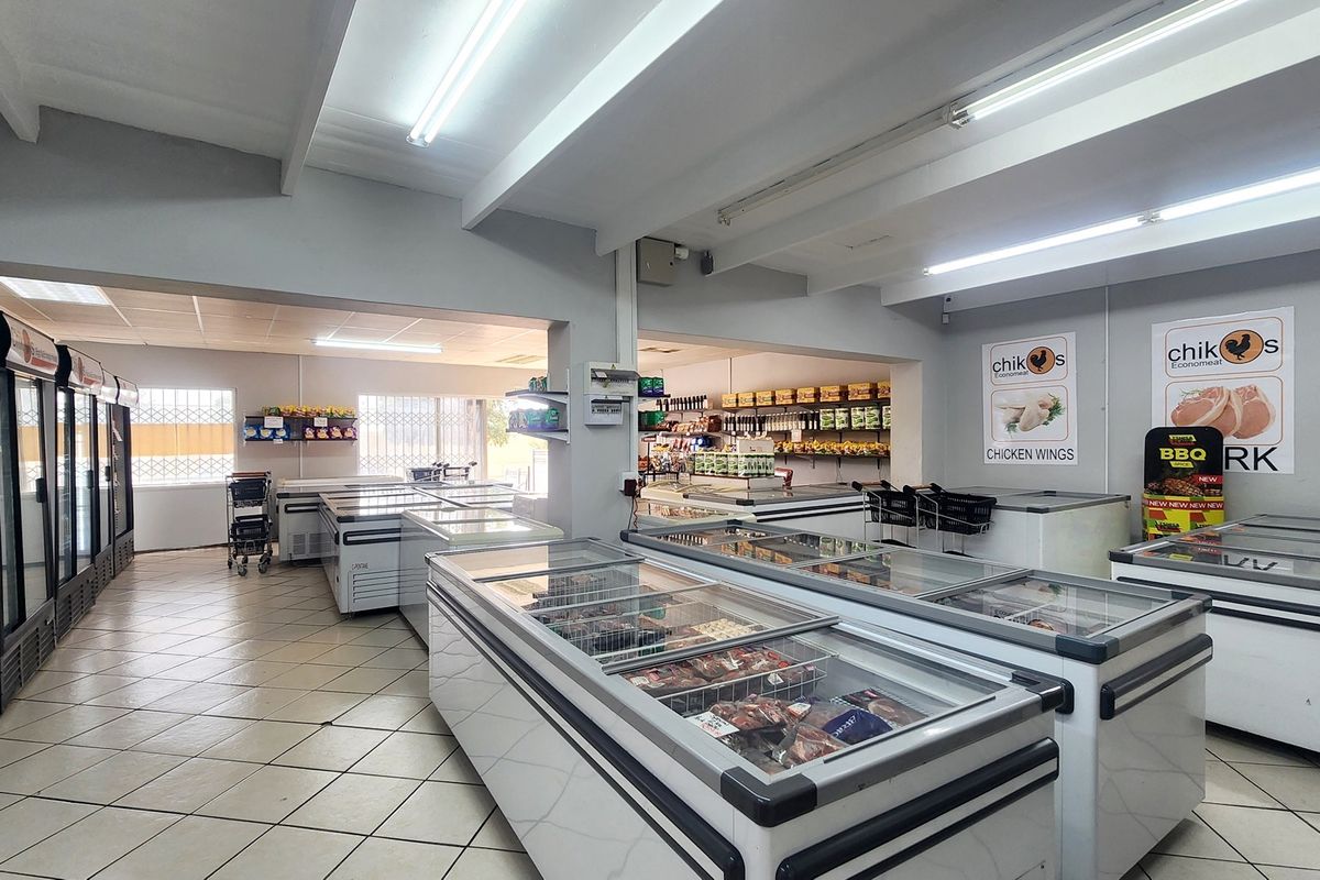 Spacious retail interior featuring tiled flooring, exposed ceiling beams, fluorescent lighting, and extensive built-in refrigeration units for commercial food display.