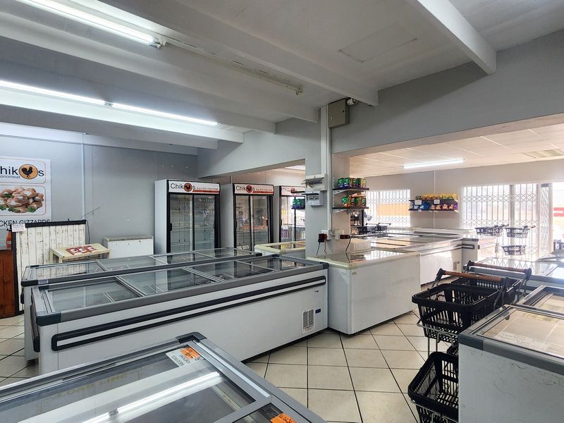A functional retail space featuring tiled flooring, commercial refrigeration units, and bright overhead lighting, suitable for a food-based retail business.