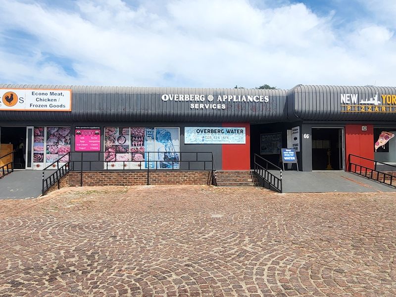 Front elevation of a retail strip center featuring multiple storefronts, paved access area, metal ramps, and prominent business signage.