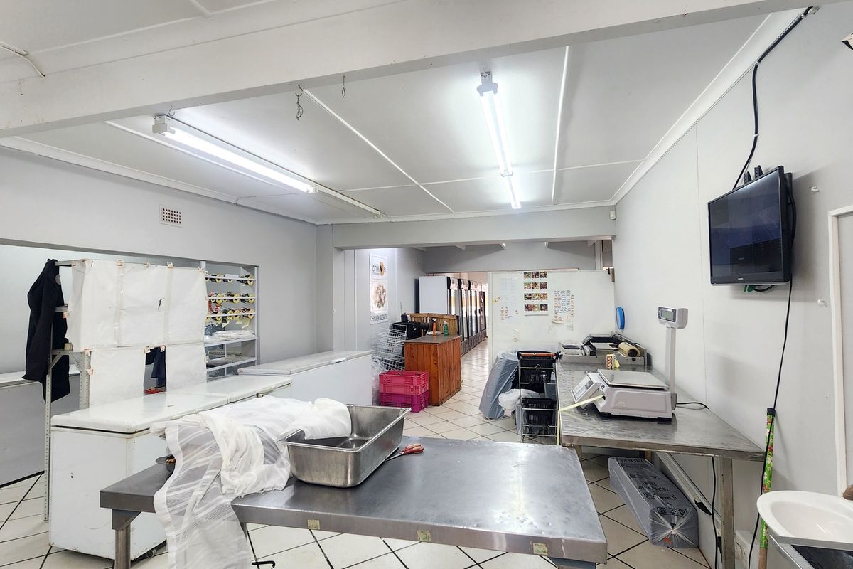 Commercial kitchen space featuring stainless steel prep tables, tiled flooring, and functional utility fixtures suitable for food preparation and retail operations.