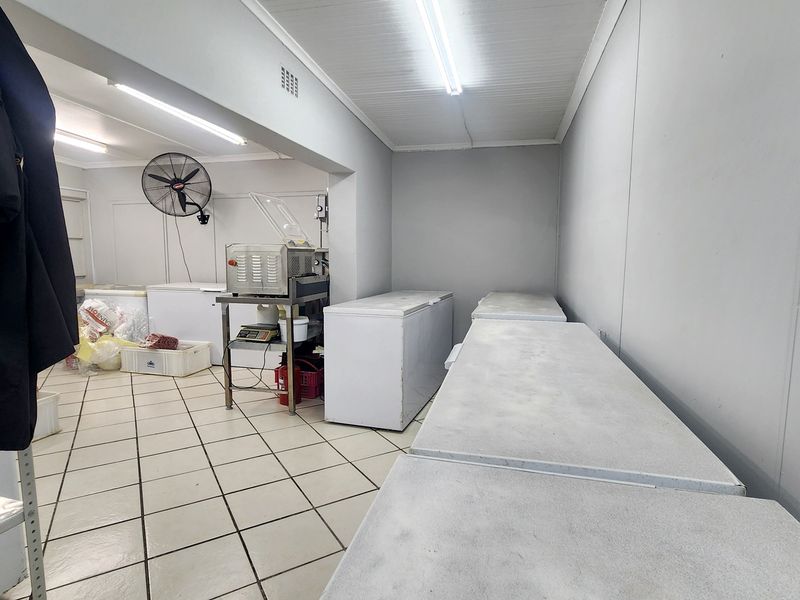 A functional utility or storage area featuring tiled flooring, fluorescent lighting, and wall-mounted ventilation, suitable for commercial preparation or storage needs.