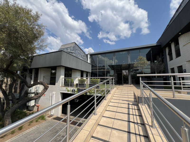 Modern office building exterior featuring a tiled access ramp with stainless steel railings, glass facade, and integrated underground parking entrance.