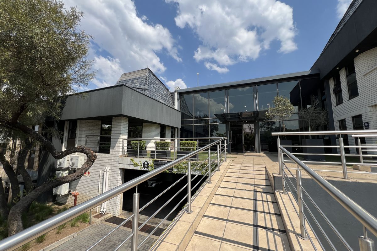 Modern office building exterior featuring a tiled access ramp with stainless steel railings, glass facade, and integrated underground parking entrance.