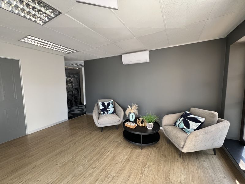 A modern office space featuring wood-look laminate flooring, a suspended ceiling with recessed lighting, and a wall-mounted air conditioning unit.