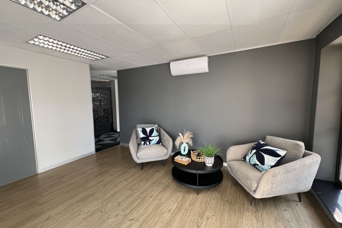 A modern office space featuring wood-look laminate flooring, a suspended ceiling with recessed lighting, and a wall-mounted air conditioning unit.