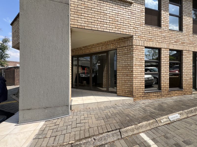 Front entrance of a modern office building featuring a face brick facade, aluminium glass doors, and a paved visitor parking area.