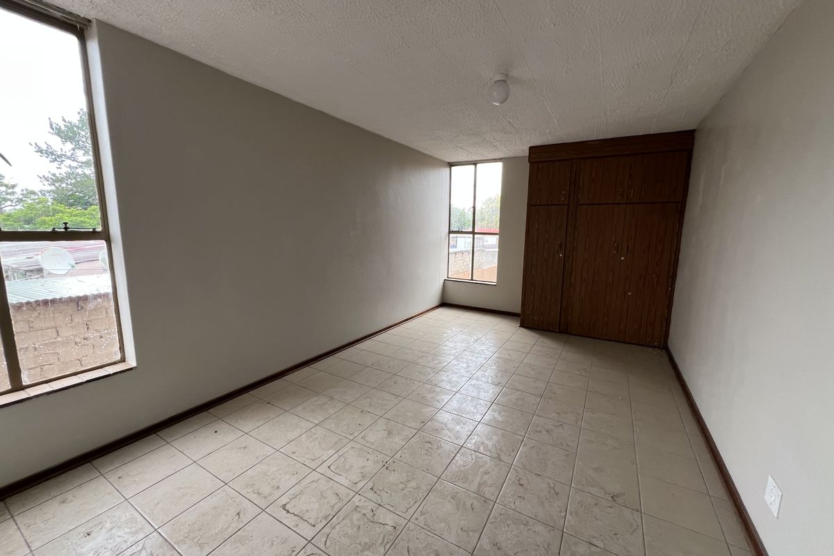 An empty bedroom featuring tiled flooring, large windows providing natural light, and built-in wooden cupboards.