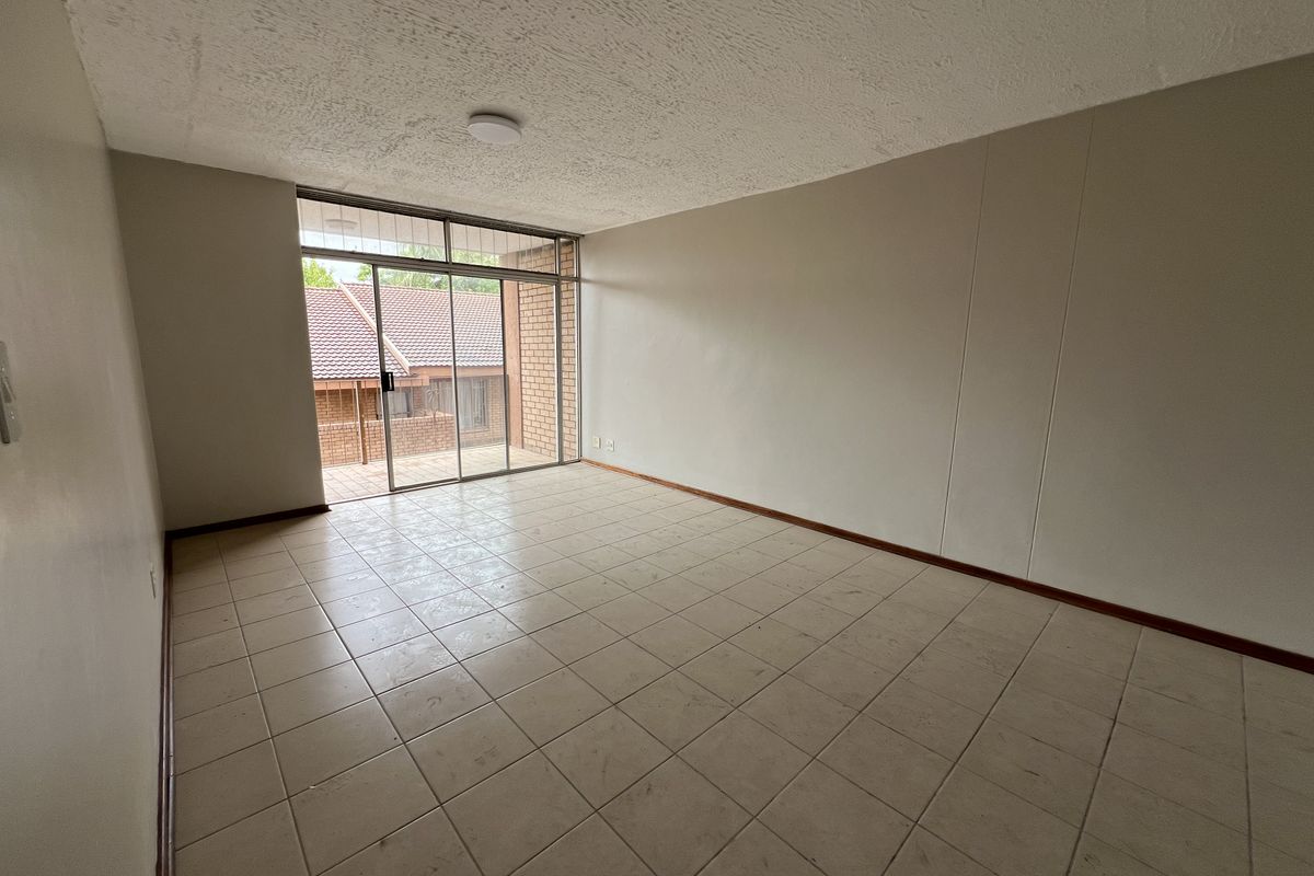 An empty living room featuring tiled flooring, a textured ceiling, and a large sliding glass door providing access to an outdoor patio area.