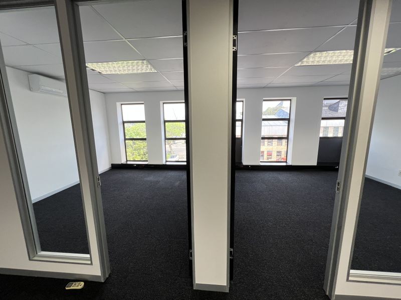 A bright, vacant commercial office space featuring suspended ceilings, recessed lighting, split-system air conditioning, and large windows providing ample natural light.