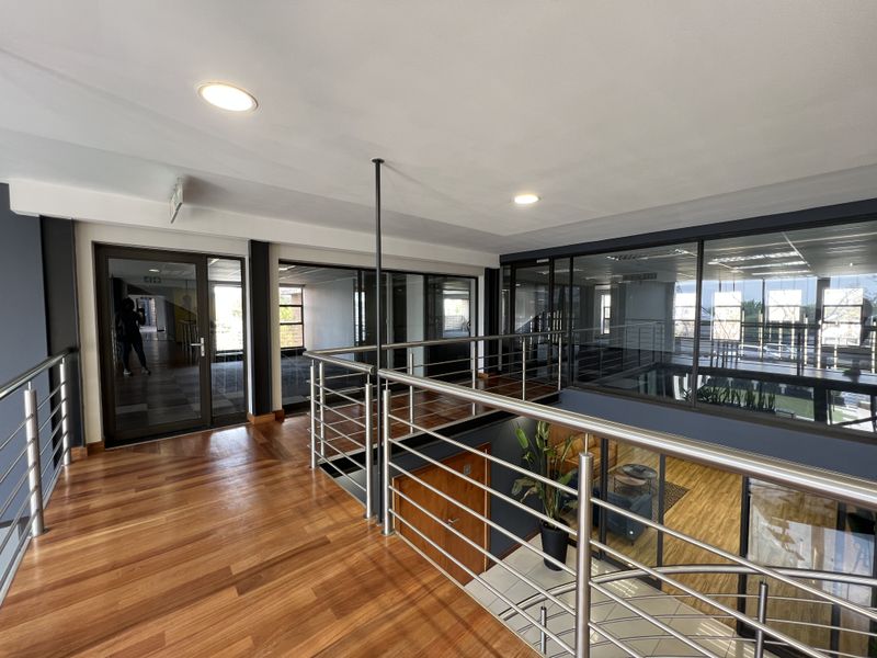 Modern commercial mezzanine hallway featuring polished hardwood flooring, stainless steel balustrades, and extensive glass partitioning for an open, professional office environment.