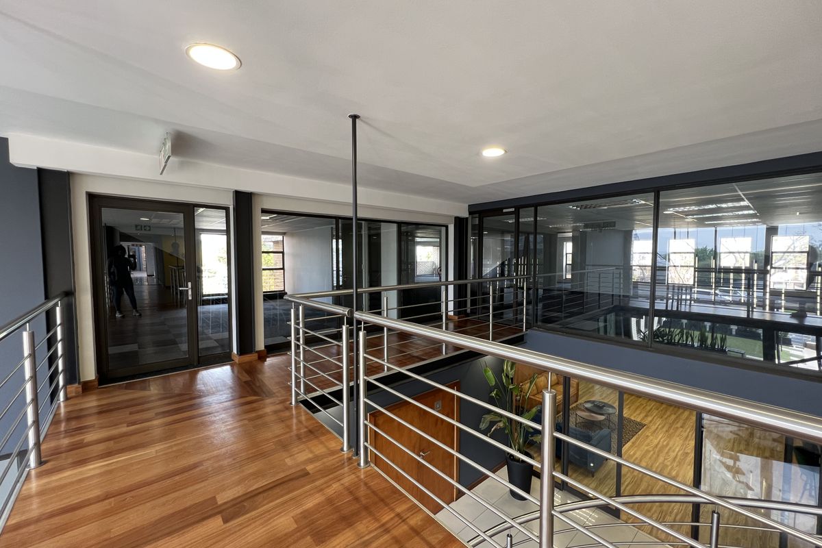 Modern commercial mezzanine hallway featuring polished hardwood flooring, stainless steel balustrades, and extensive glass partitioning for an open, professional office environment.