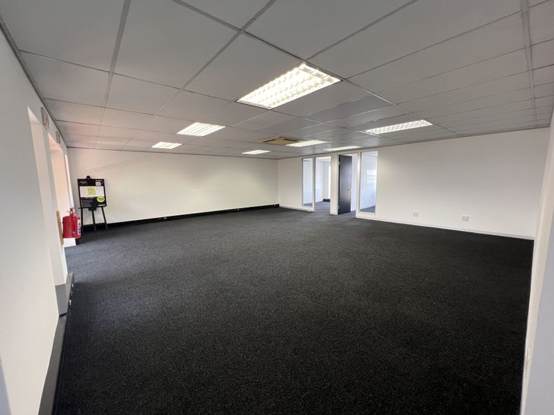 A spacious, open-plan commercial office area featuring a suspended ceiling, recessed lighting, and dark carpeting, offering a clean and professional workspace.