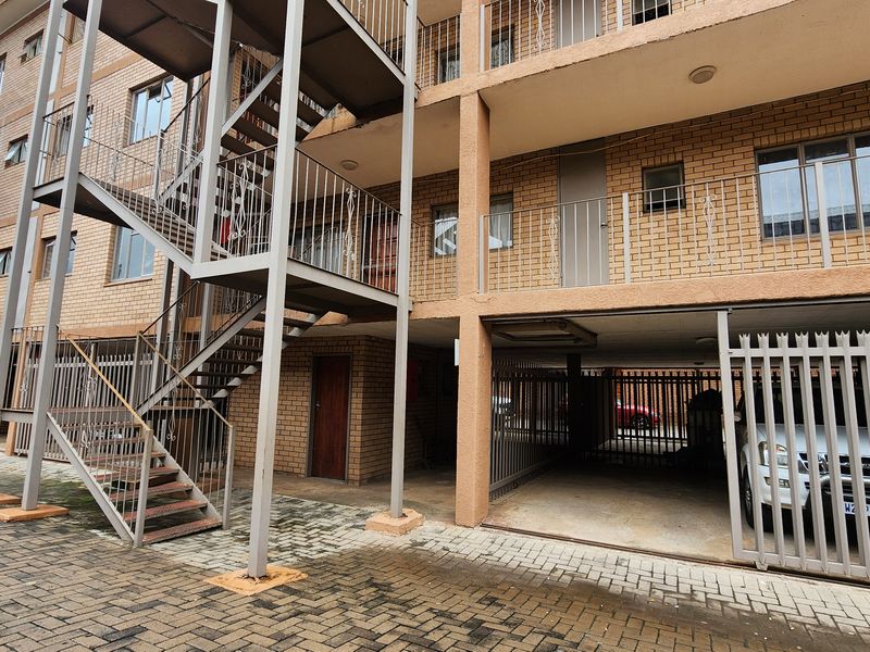 Exterior view of an apartment building featuring a brick facade, open-air metal staircase, and ground-level covered parking area with security gates.