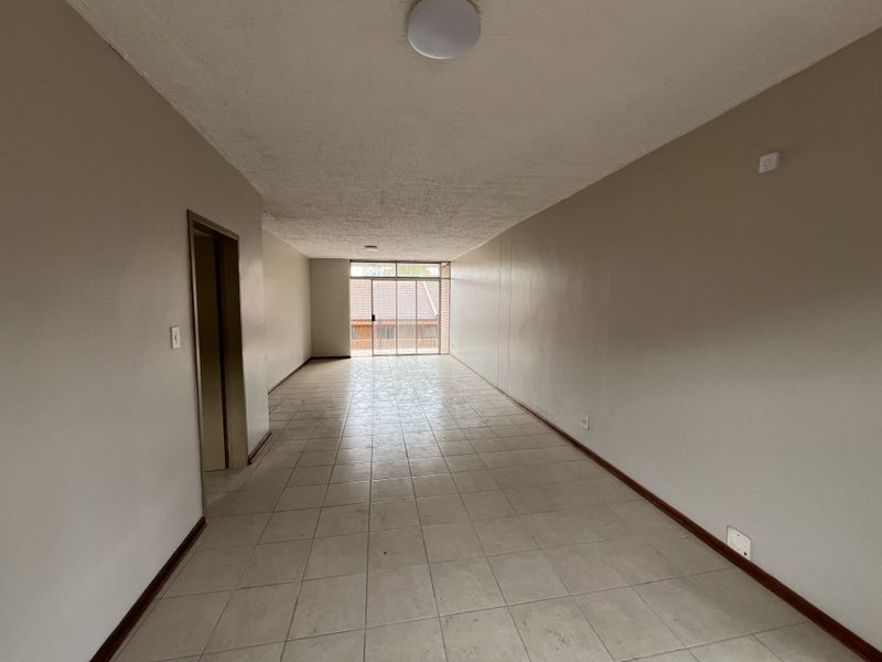 An empty, open-plan living area featuring tiled flooring, neutral walls, and a large sliding glass door providing access to the exterior.